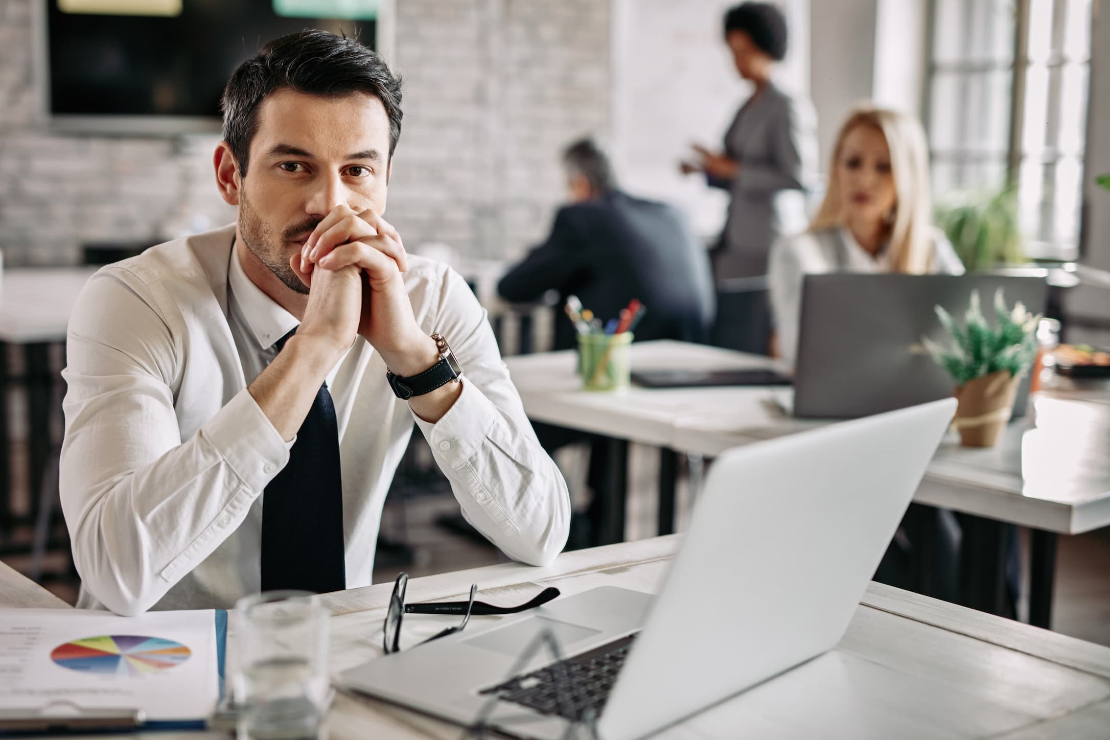 Hombre de negocios pensativo trabajando en la oficina con gente al fondo